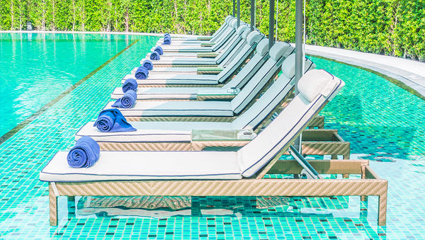 white sun loungers lined beside a swimming pool with rolled towels in a resort setting