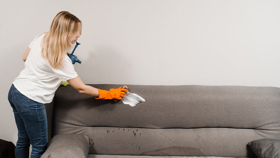 Woman cleaning a fabric sofa with a brush and cleaning solution, removing stains from upholstery