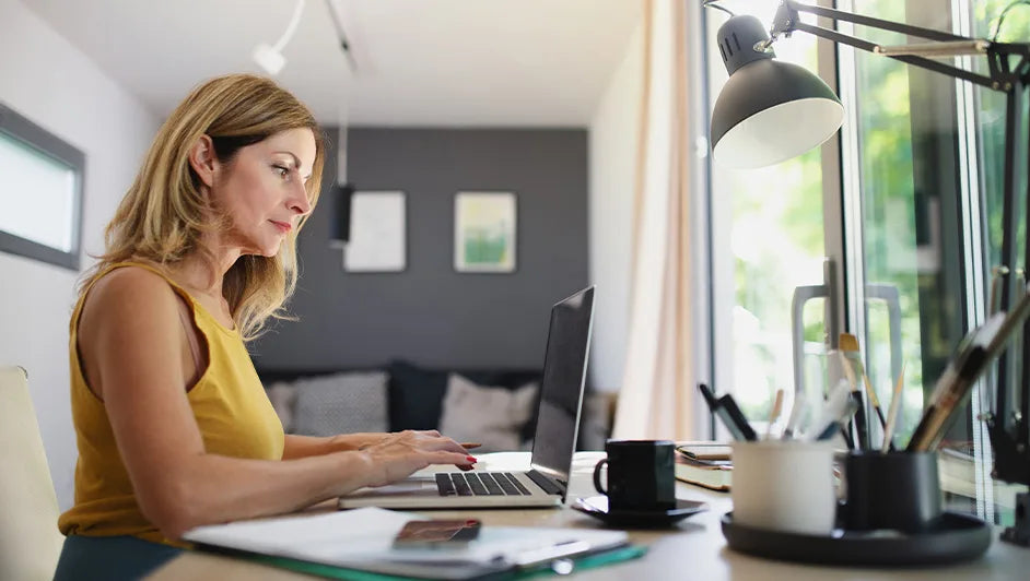 A woman working on a laptop in a bright home office near a window, showcasing modern Australian lifestyle furniture.