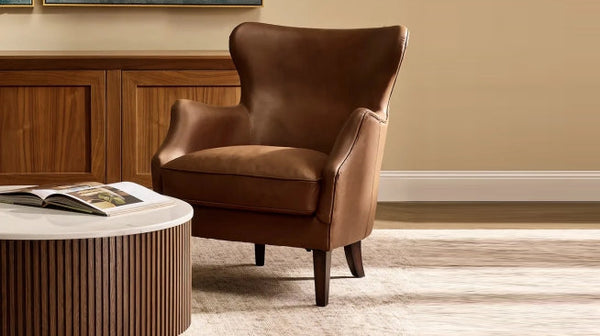 Close-up of a classic brown leather wingback armchair next to a round, slatted wood and marble coffee table