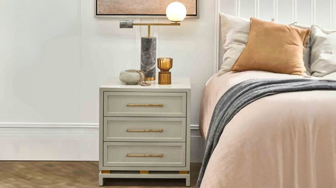 Modern bedside table with lamp, decor pieces, and a neatly styled bed with cushions and throw blanket.