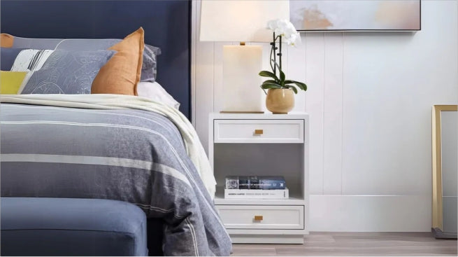Modern white bedside table with lamp and books next to a stylish bed